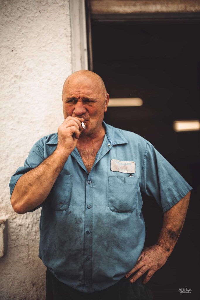 Documentary-style portrait of an older man smoking outside in work clothes.